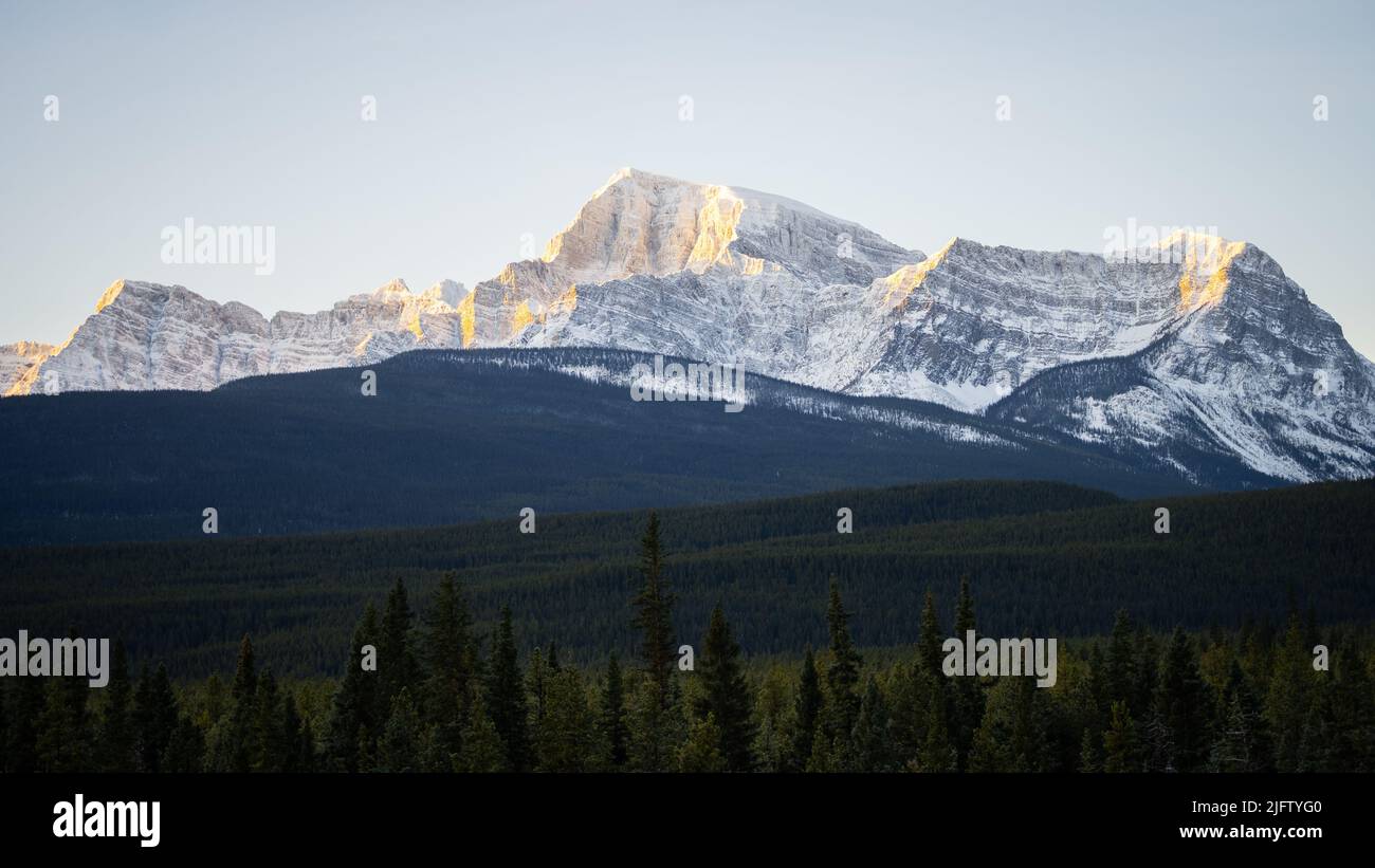 Massive rocky mountain catching the first sun rays on a cold winter morning, wide, Banff NP, Canada Stock Photo