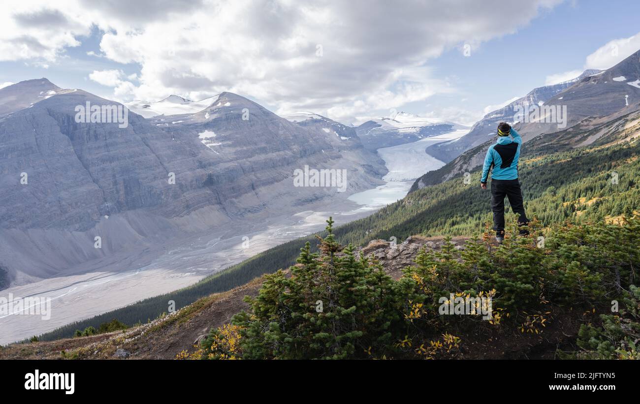 Male hiker overlooking untouched alpine valley with glacier on its end, Jasper, Canada Stock Photo