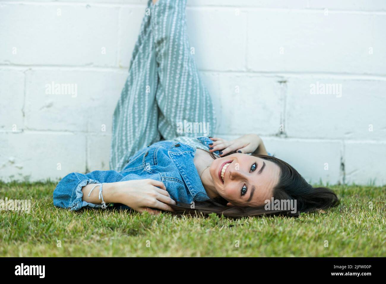 A teenage girl lying on the ground with her legs propped up on a wall with a happy look for a cool angle with copy space for text Stock Photo