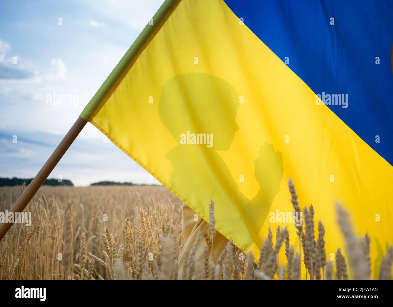 silhouette of a child standing behind the national blue and yellow flag in a wheat field, praying for Ukraine. no war, stop aggression. Ukrainian chil Stock Photo