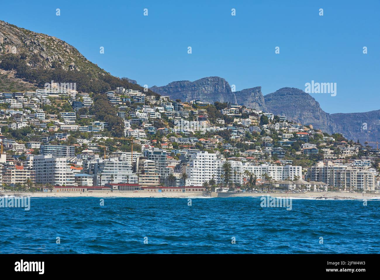 Panorama seascape with clouds, blue sky, and fancy hotel apartment buildings in the background. Sea Point with the Twelve Apostles and Table Mountain Stock Photo