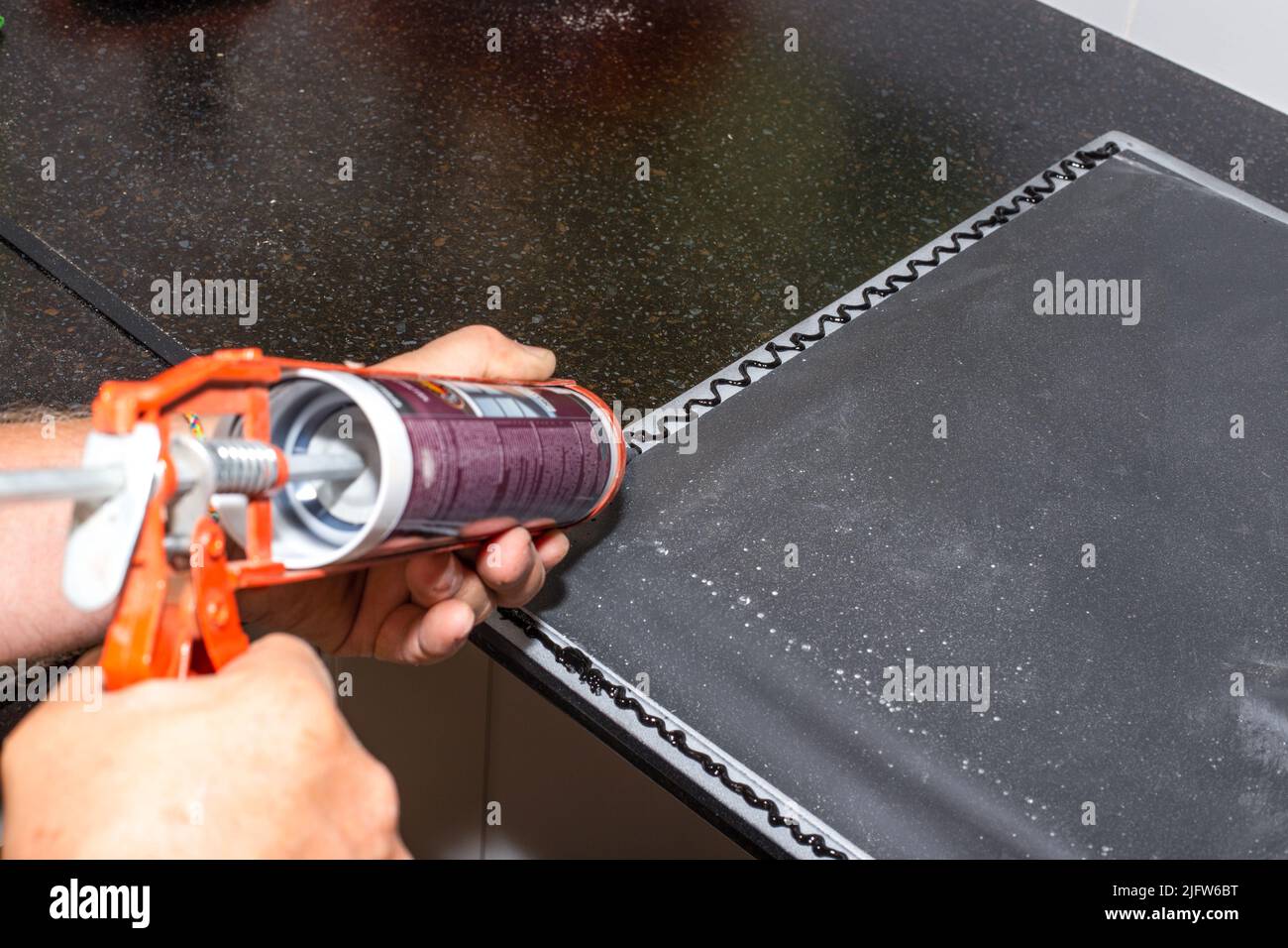 Applying black sanitary sealant with a nail gun to the edge of the kitchen sink. Installing a