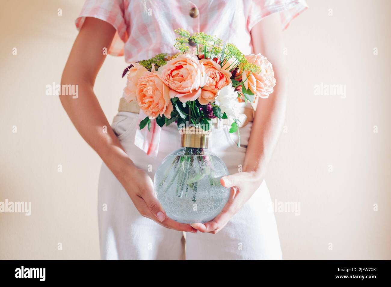 Close up of summer bouquet of flowers in transparent glass vase. Woman florist holds arrangement with orange roses Stock Photo