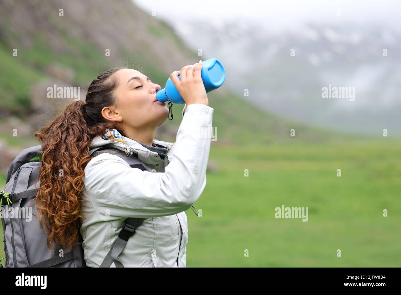 Trekker drinking water from canteen standing alone in the mountain a foggy day Stock Photo