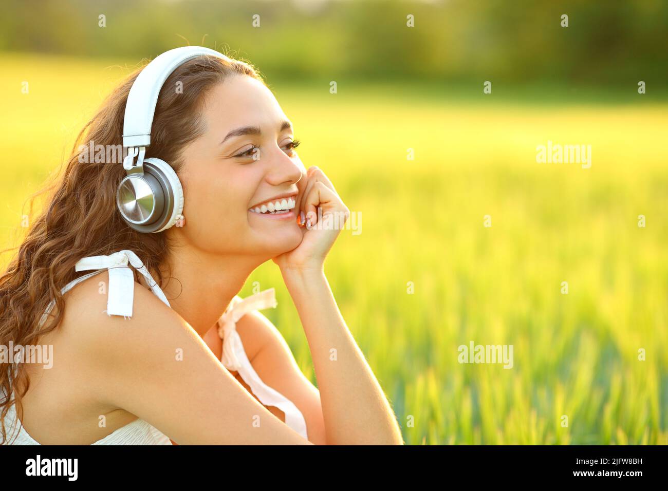 Happy woman listening to music with wireless headphones sitting in a wheat field Stock Photo
