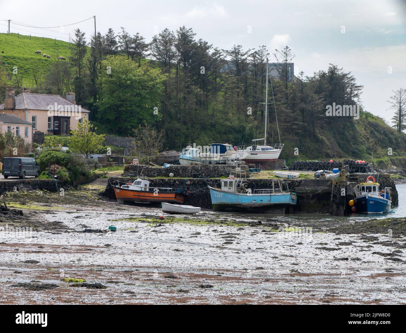 West Cork, Ireland, April 30, 2022. The exposed seabed at low tide. Small fishing boats on the shallows. Sea mud. A pier for fishing boats. Coastal in Stock Photo