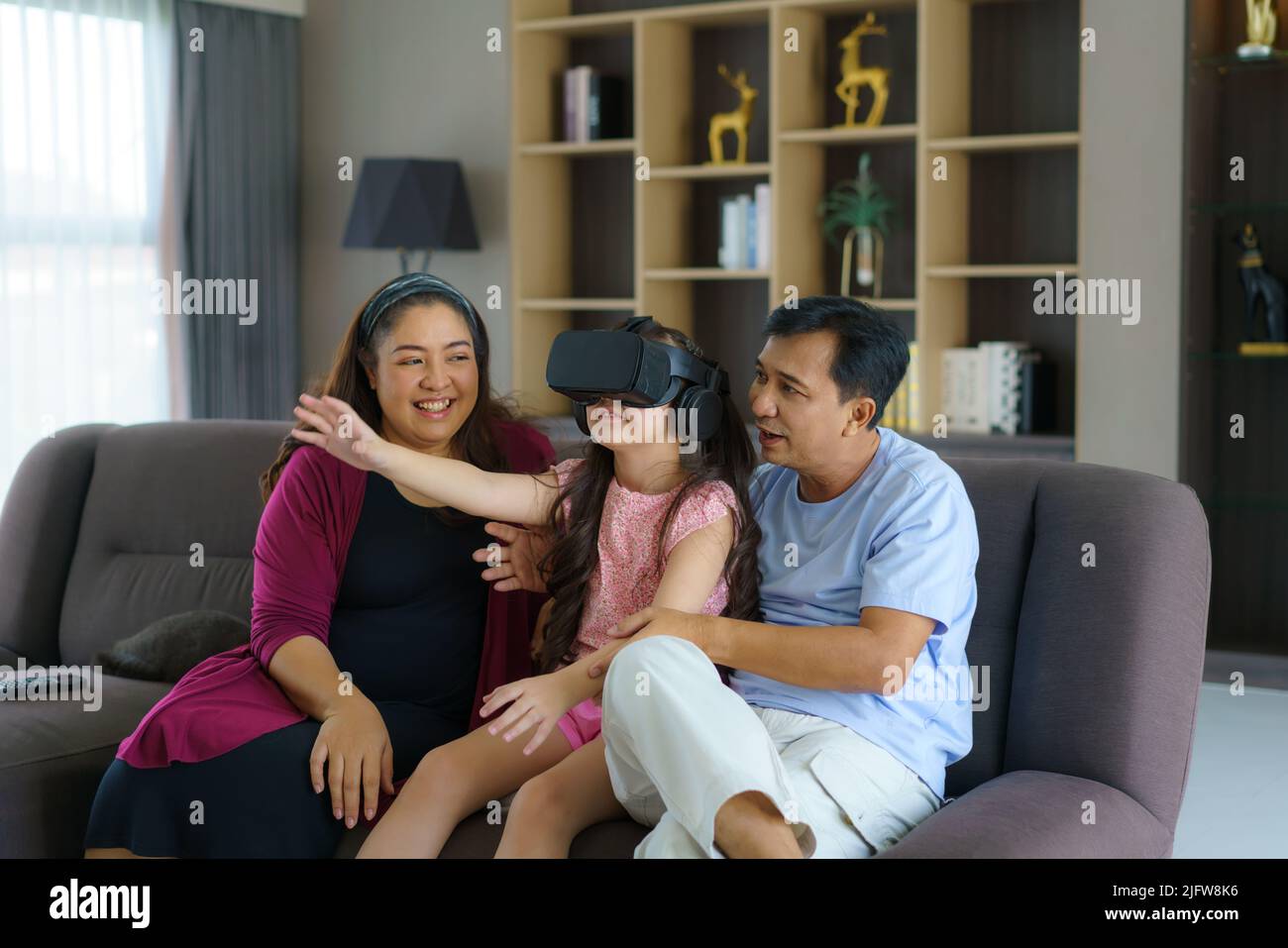 Asian family enjoy technology device hand use vr goggle glasses play fun together on sofa living room at home. Smart technology with lifestyle. Stock Photo