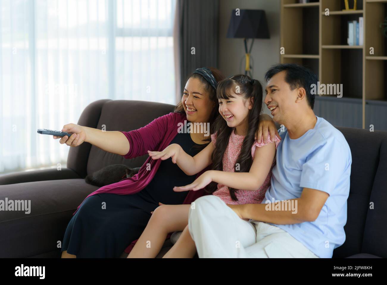 Happy Asian family with father, mother and daughter enjoy weekend activity spending more time at home and therefore probably more time in front of the Stock Photo