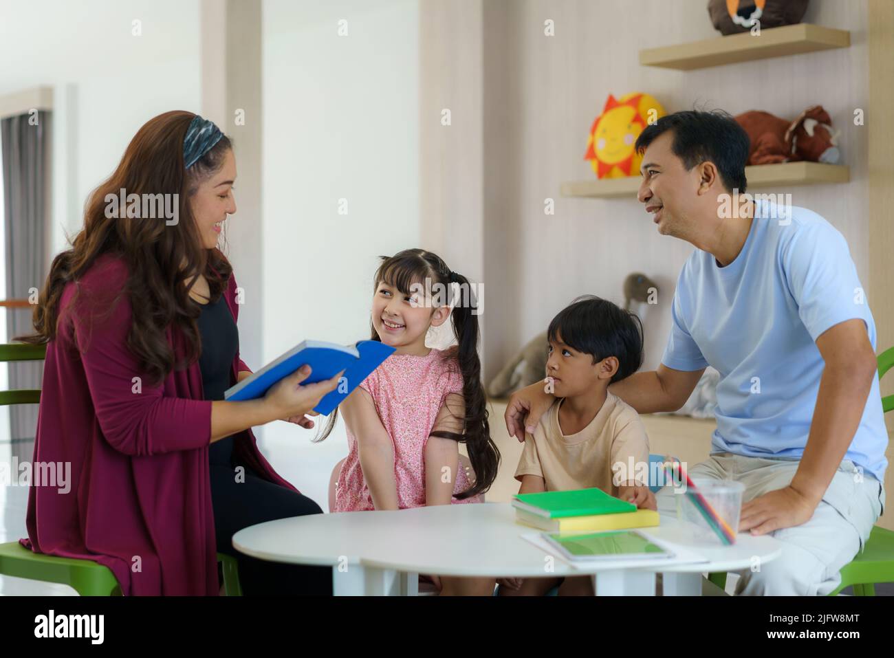Happy Asian family sitting on chair reading a book together in the living room at home  for they education when spend their family time. Stock Photo