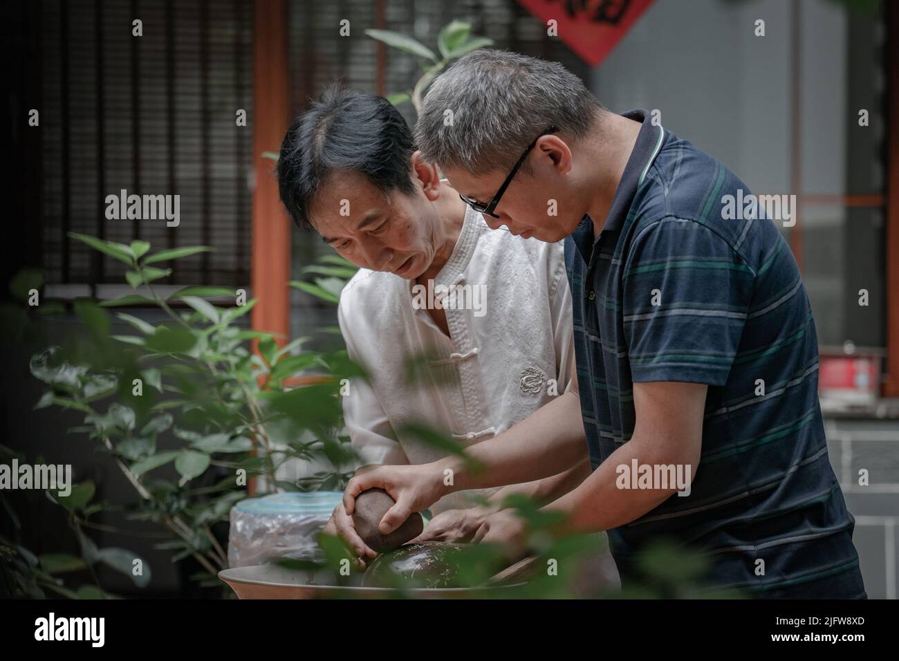 (220705) -- KUNMING, July 5, 2022 (Xinhua) -- Xu Ronghong (L), a Zitao (purple pottery) craftsman, teaches an apprentice to polish a pottery ware in Wanyao Village of Jianshui County, Honghe Hani and Yi Autonomous Prefecture, southwest China's Yunnan Province, June 30, 2022. Xu Ronghong, 57, is an inheritor of the making skills of Jianshui purple pottery, one of the national intangible cultural heritages of China. Xu was born in Jianshui County. As the fifth generation pottery maker of his family, Xu started to learn the techniques since childhood. In order to make an excellent piece of p Stock Photo