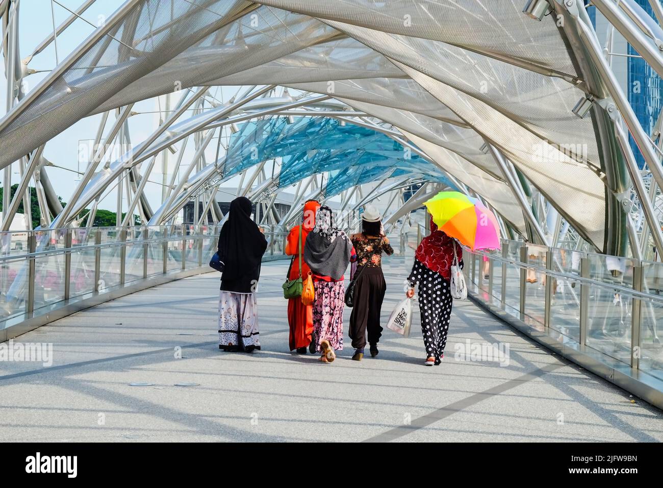 Group of fashionable Asian women in bright beautiful national dresses crossing famous DNA footbridge,The Helix bridge Stock Photo