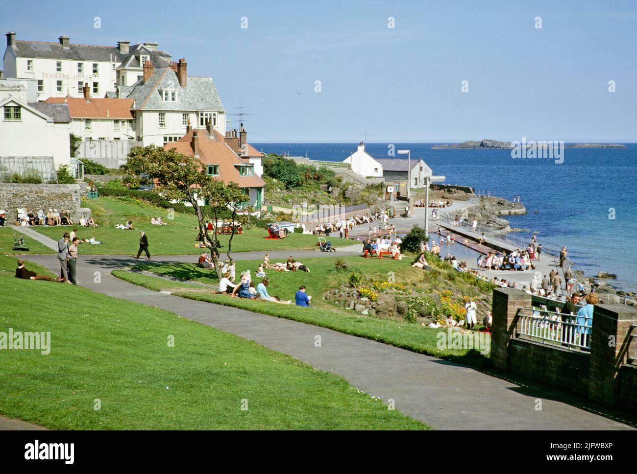 People sittng on grass by the coast enjoying sunshine at the seaside resort of Portrush, County Antrim, Northern Ireland, UK 1960s Stock Photo