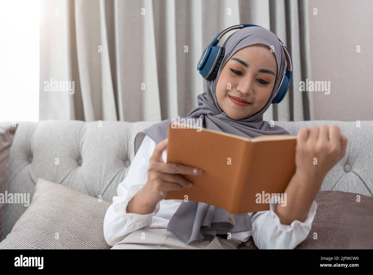 Cozy stay at home activities. young woman in hijab reading her favorite ...