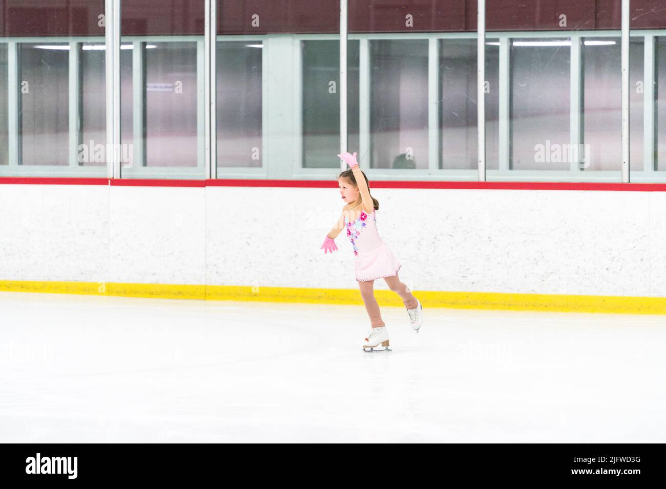 Little girl practicing figure skating on an indoor ice skating rink