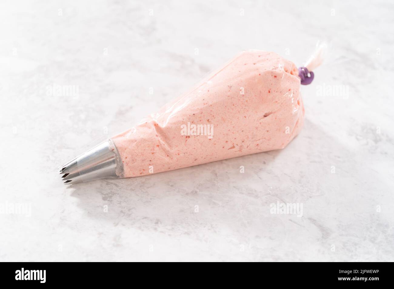 Strawberry buttercream frosting in a piping bag with a large metal