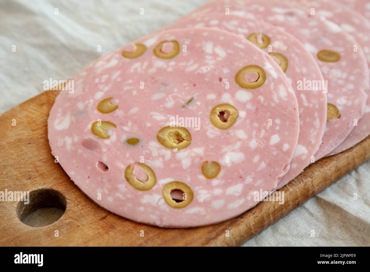 Organic Sliced Mortadella Sausage with Olives on a rustic wooden board, side view. Closeup