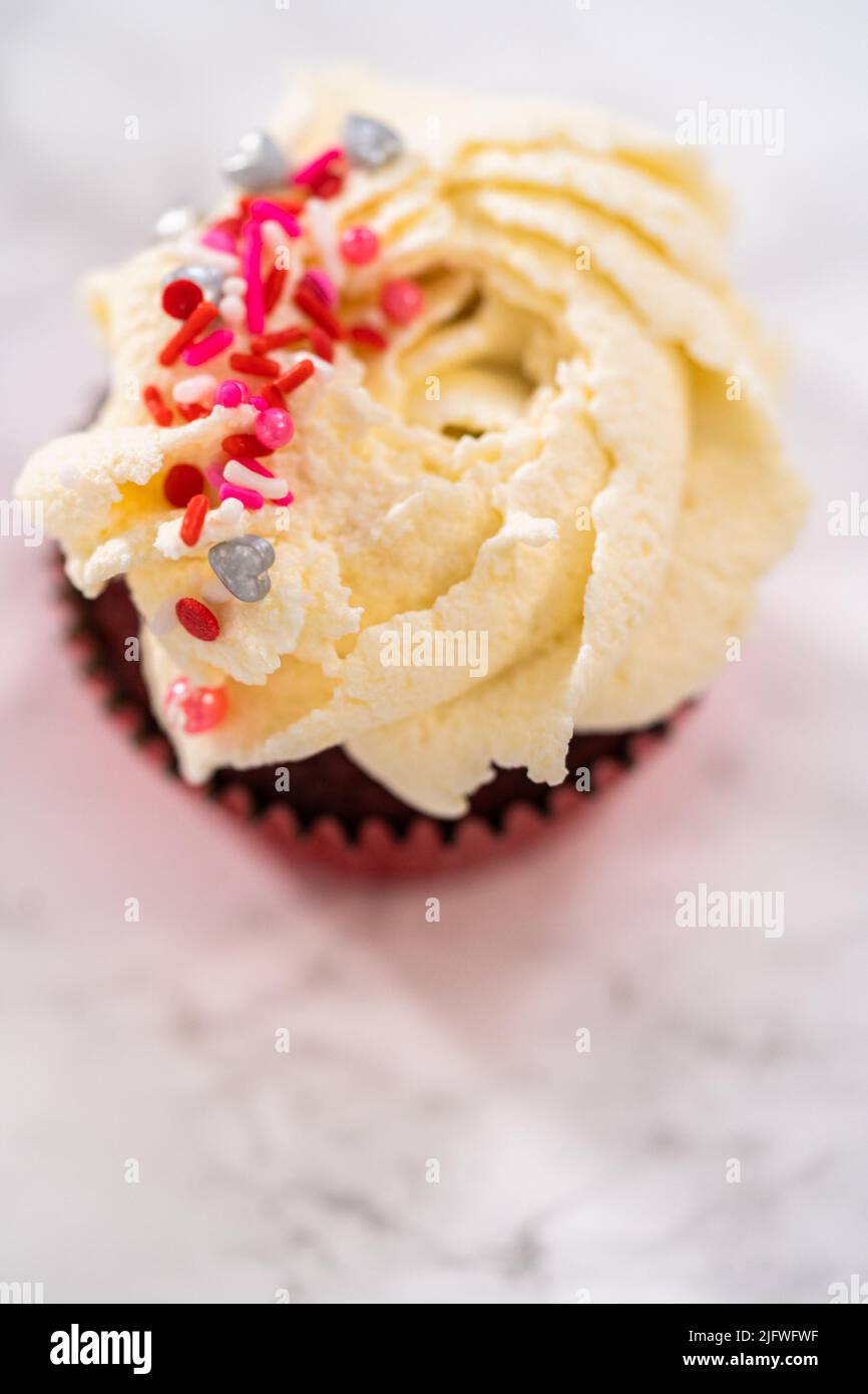 Piping white chocolate ganache frosting on top of red velvet cupcakes