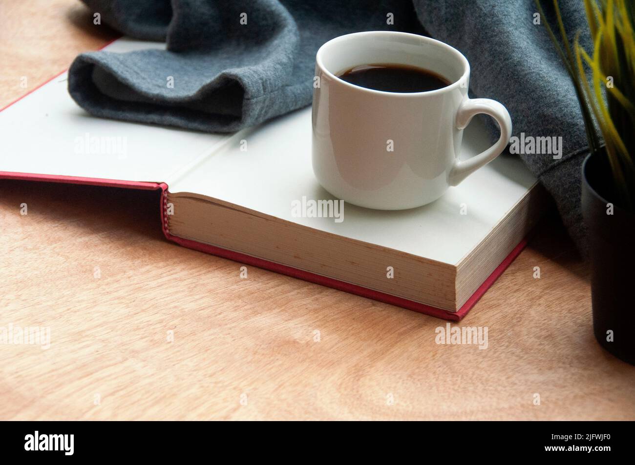 Coffee cup on top of a book with grey jacket on wooden desk background. Directly view. Copy space. Stock Photo