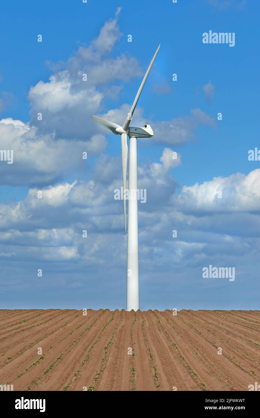 Wind turbines on a farm with newly planted crops. Cloudy day on agricultural land where wind energy is the main resource. Producing sustainable Stock Photo