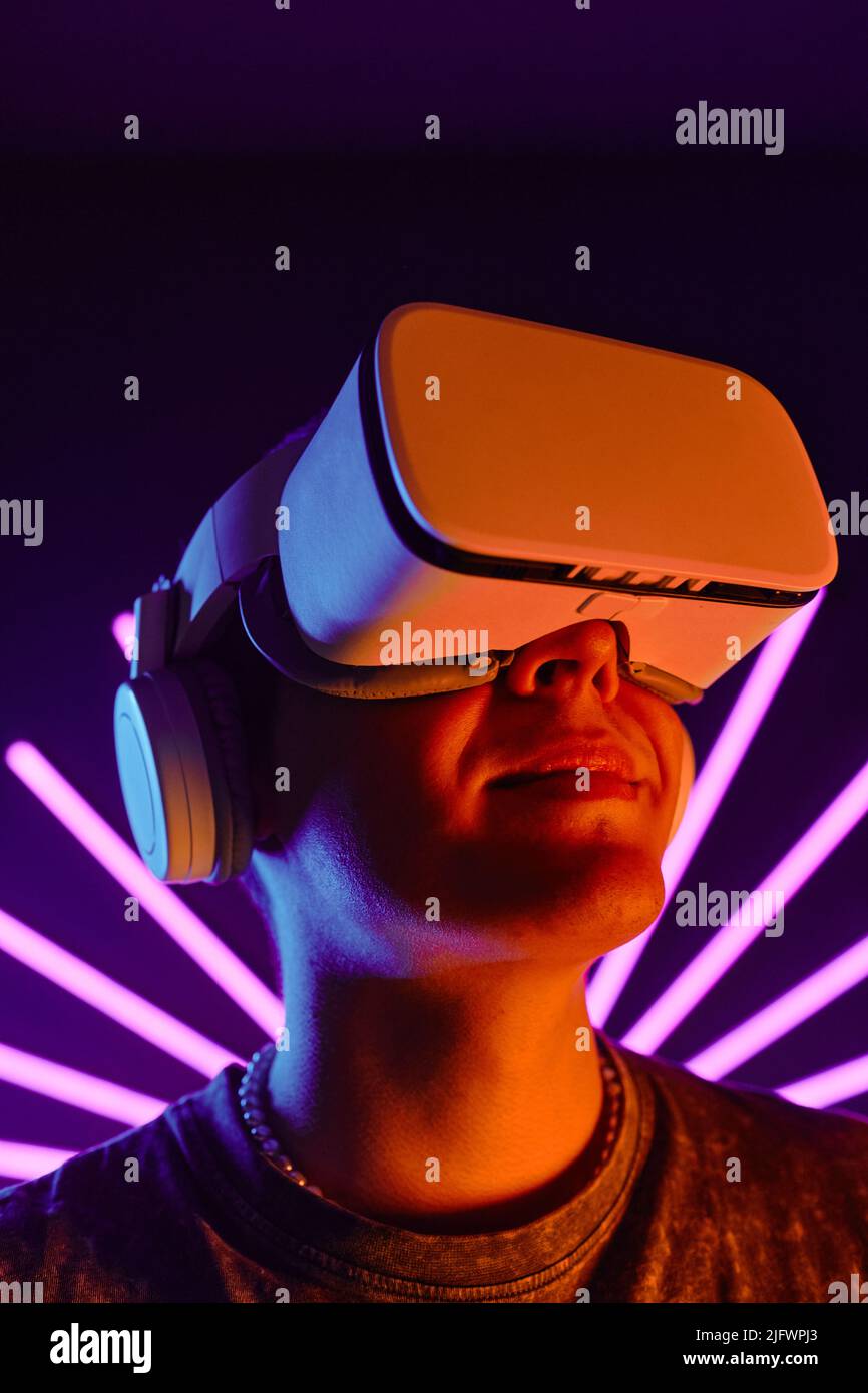 Futuristic portrait of smiling man wearing VR headset with neon light beams in background Stock Photo