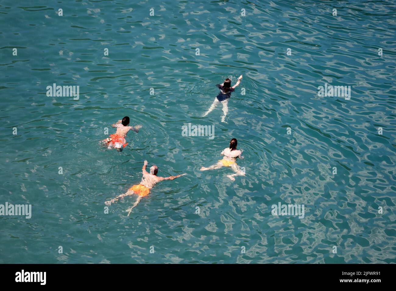 Aerial view to azure sea and group of people swimming in transparent water. Men and women swimmers, beach vacation in summer Stock Photo
