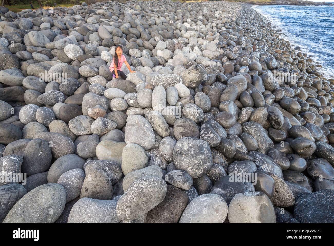 A young girl (MR) on a south facing beach near Nuu Bay with huge stone boulders, Maui, Hawaii. Stock Photo