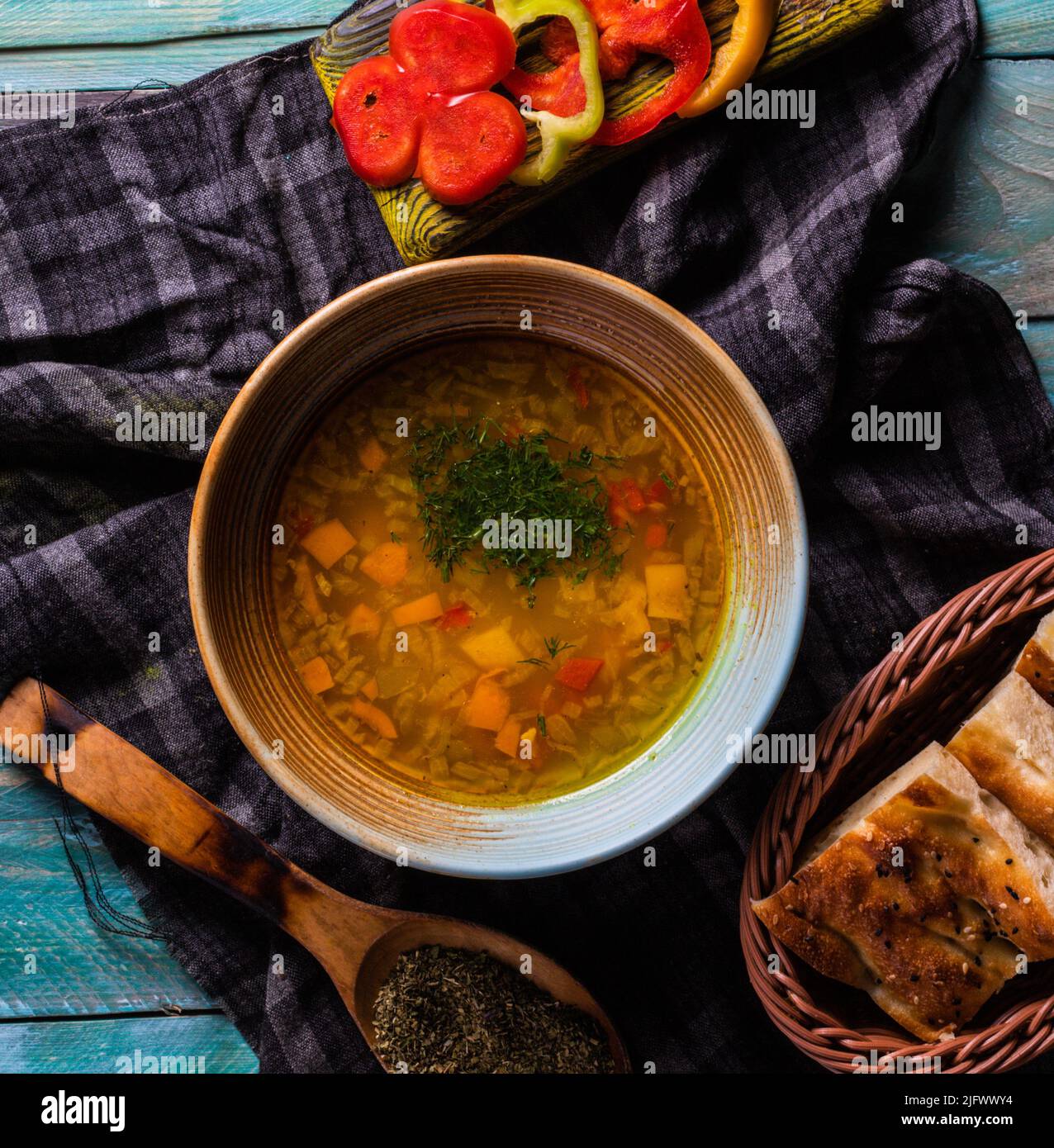 A top view of a bowl of vegetable soup surrounded by sliced pepper and species on a cloth on a