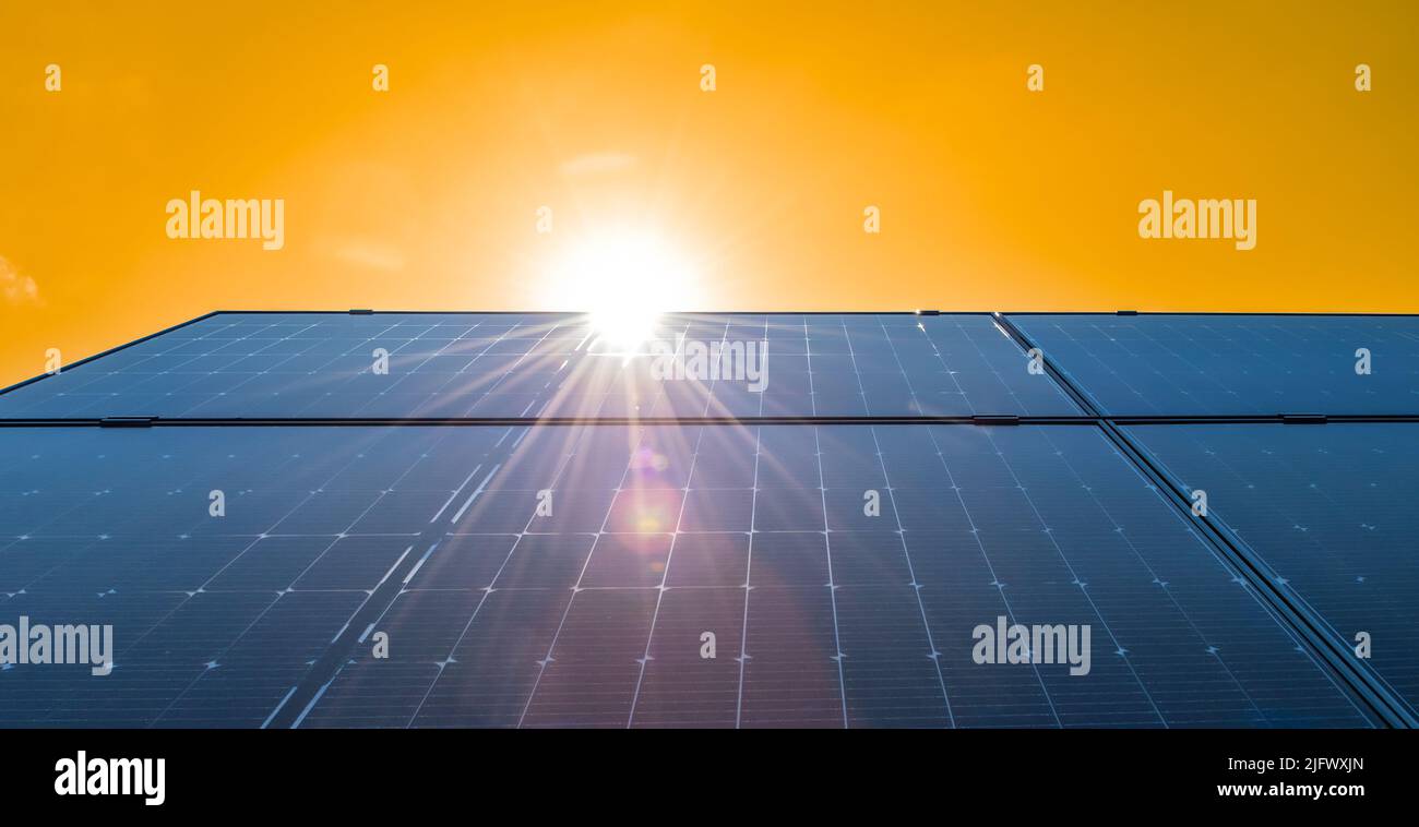 Solar panels on roof against bright yellow sky background. Stock Photo