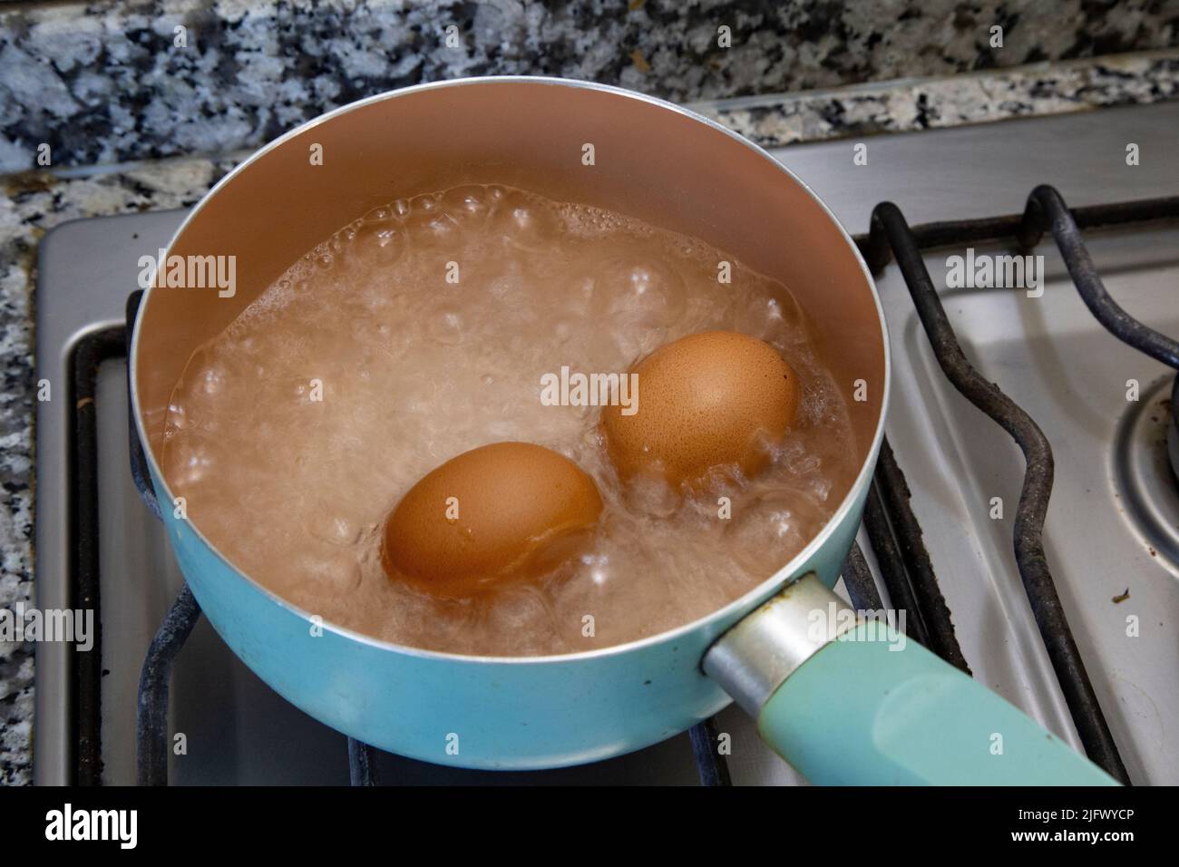 Chicken eggs boiling in water in a light blue saucepan on the stove