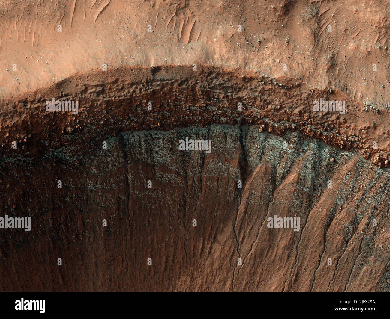 Every winter carbon dioxide frost (dry ice) forms on Mars' surface. At its greatest extent this frost reaches from the poles to mid latitudes until it is too warm/sunny to persist. In most places this is around 50 degrees latitude, although small patches of dry ice are found closer to the equator on colder, less sunny, pole-facing slopes. This image was taken in the middle of winter in Mars' southern hemisphere. The south-facing slope has patchy frost, blue in enhanced colour. Image is less than 1km across.  An optimised and enhanced version of NASA imagery. Credit: NASA/JPL/UArizona Stock Photo