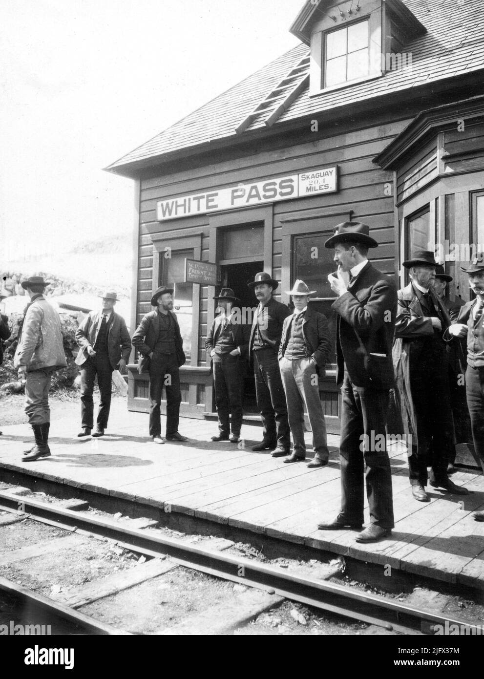 Historical image. Klondike Goldrush, 1900. Gentlemen and prospectors standing at the White Pass & Yukon Railroad Station in Alaska. The station was a main point for prospectors to head off to the goldfields of Alaska and Yukon which, unbeknownst to them, already had seen most of the good Klondike claims staked out.The gentleman in white hat is Sidney Paige, a geologist of the US Geological Survey who was also exploring the area and inventorying the minerals for the USGS. Credit: USGS. Stock Photo