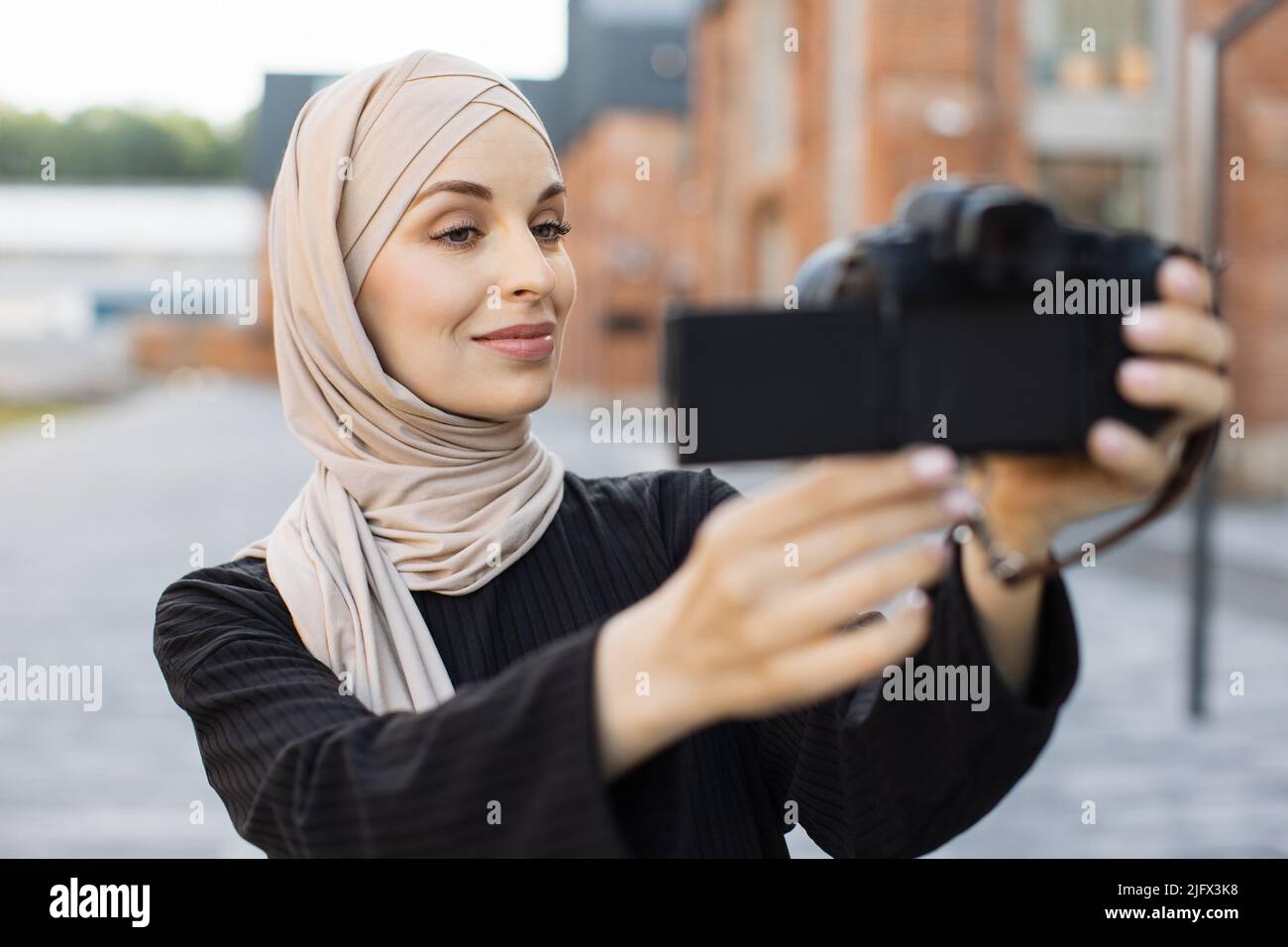 Young female muslim blogger in trendy clothes and hijab walks on city ...
