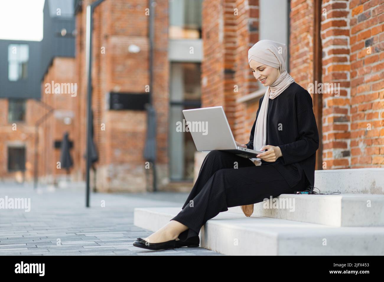 Pretty smiling muslim business woman in hijab sitting on stairs and ...