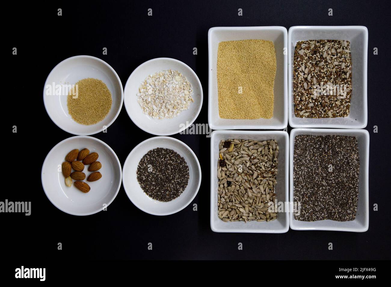 Dark background with white bowls contain healthy seeds for a vegan diet Stock Photo