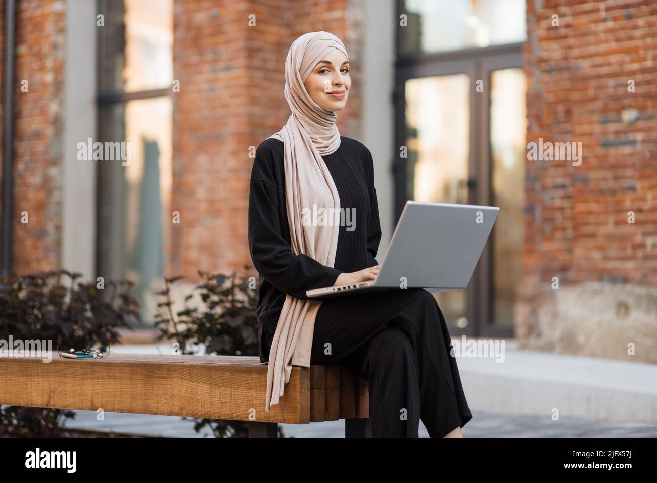 Pretty smiling muslim business woman in hijab sitting on bench and ...