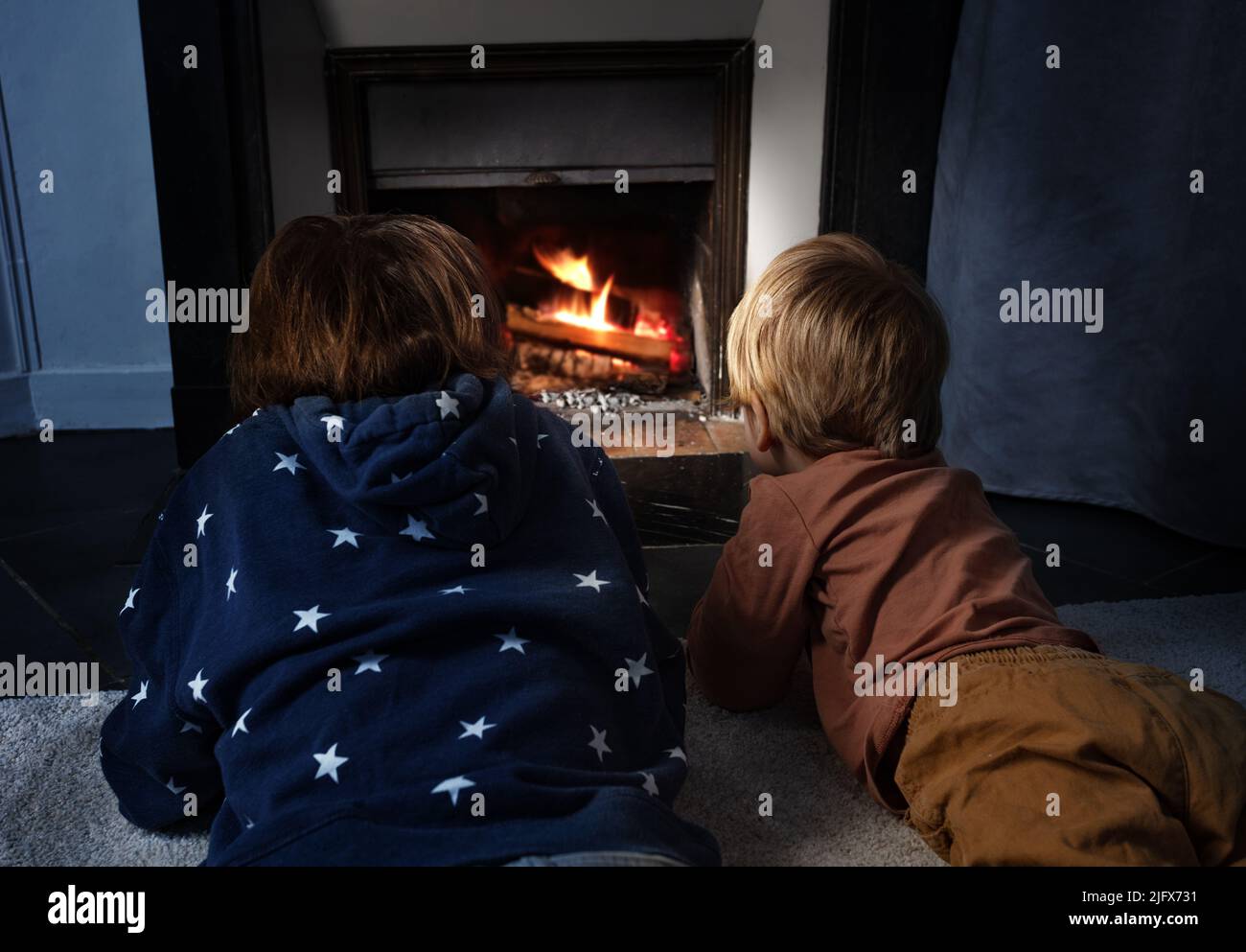 Two boys lay in front of the home fireplace look at fire Stock Photo