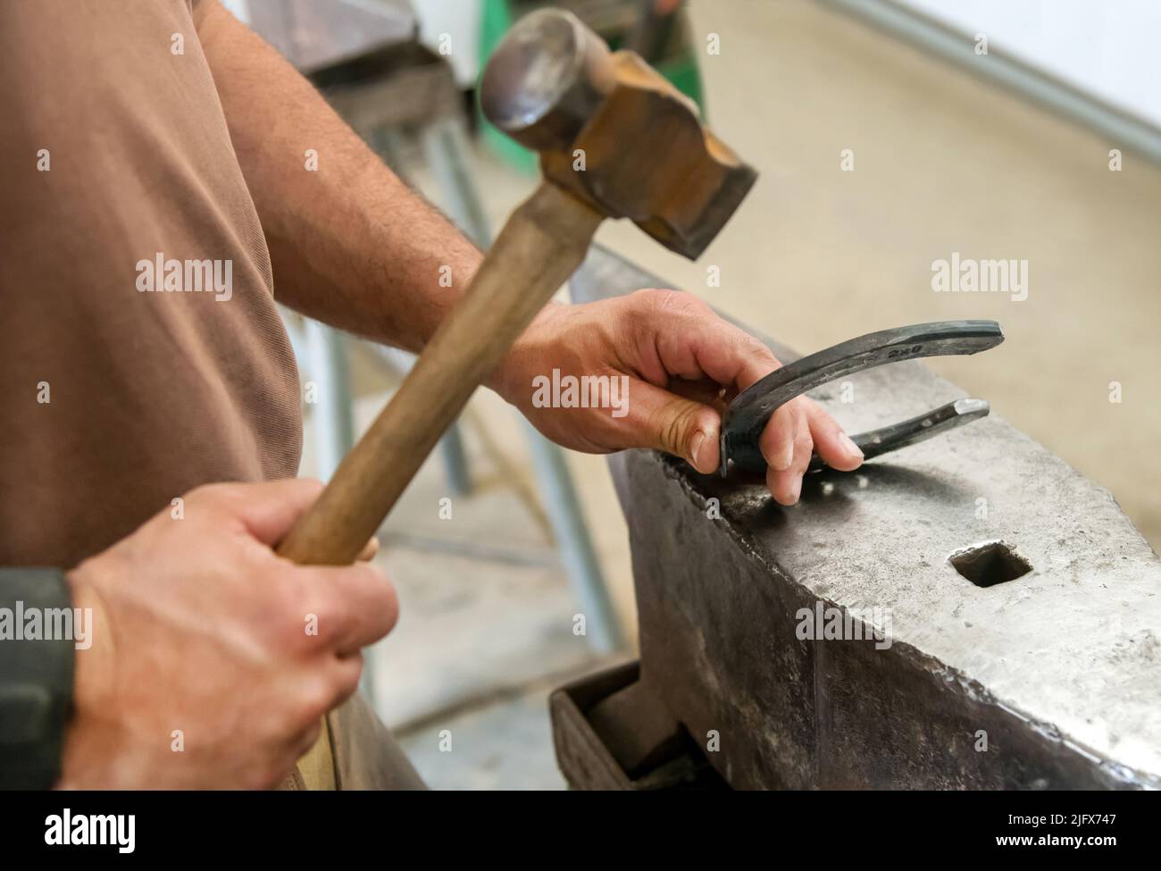 From above anonymous man hitting iron horse shoe with hammer on anvil while working in workshop on ranch Stock Photo