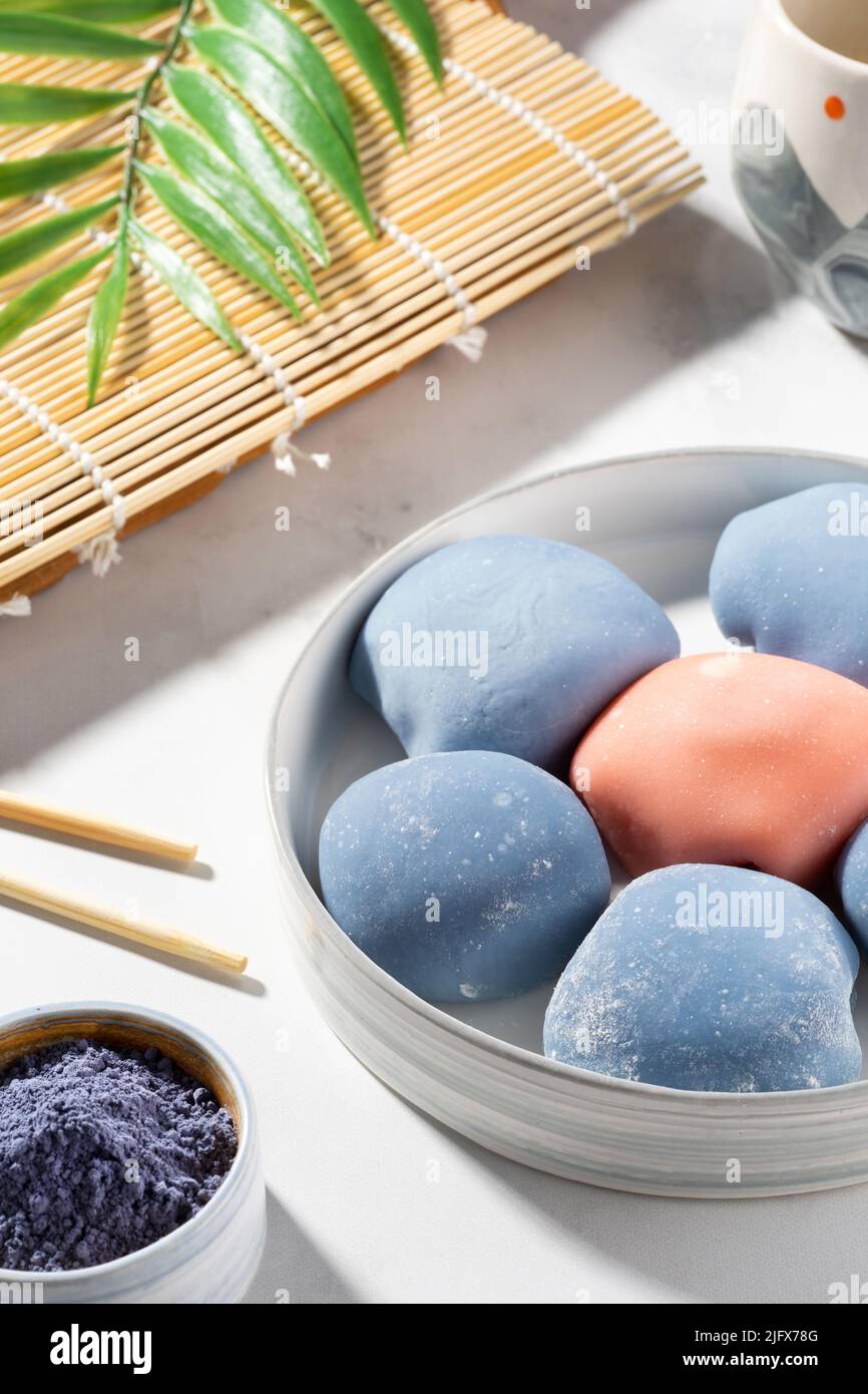 Concept of a traditional Japanese dessert on the kitchen table. A bowl of Japanese mochi with chopsticks and wooden mat on white countertop. Stock Photo