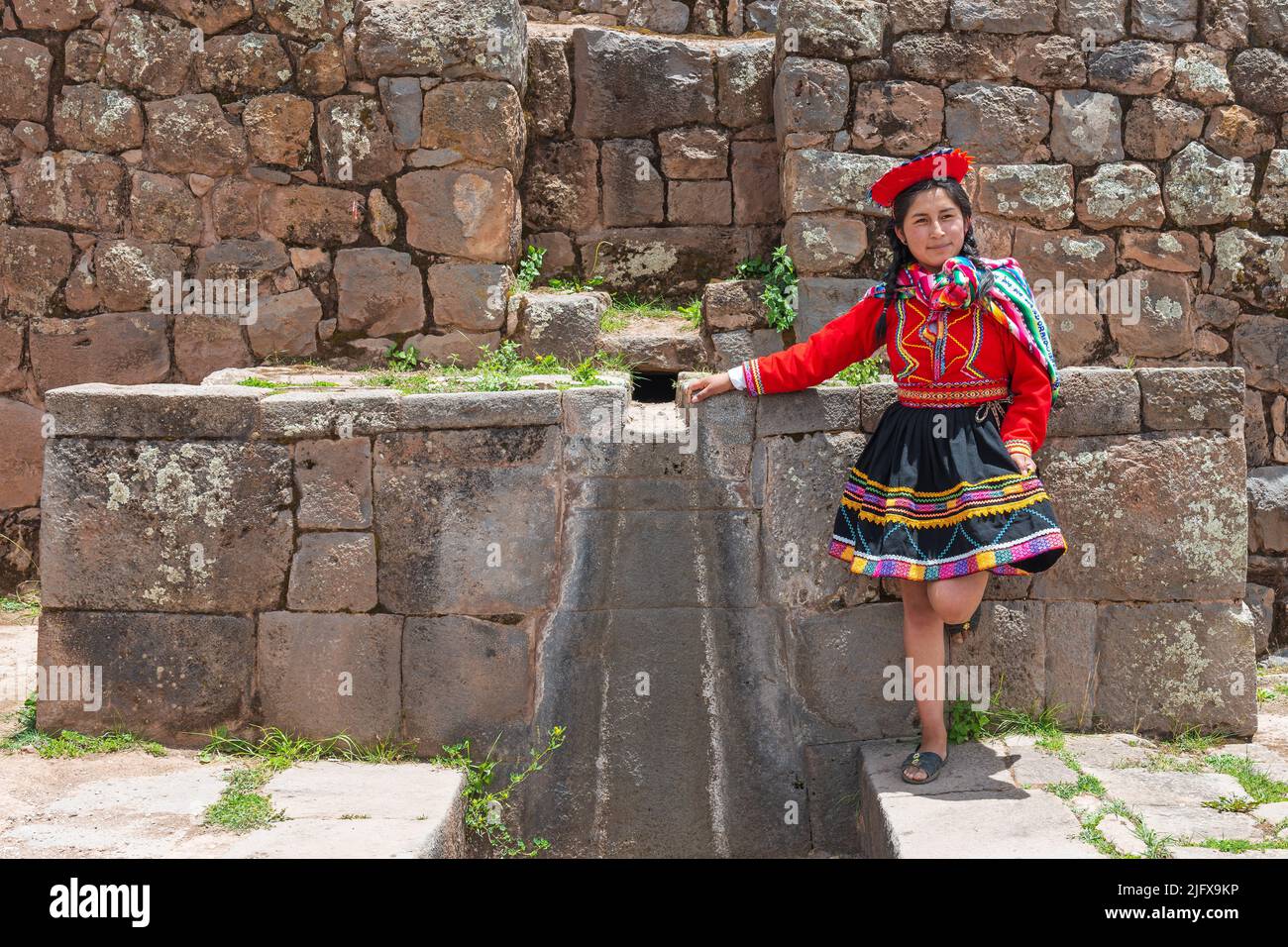 Peruvian indigenous Quechua woman by a inca wall with fountain in the Sacred Valley of the inca in Tipon near Cusco, Peru. Stock Photo
