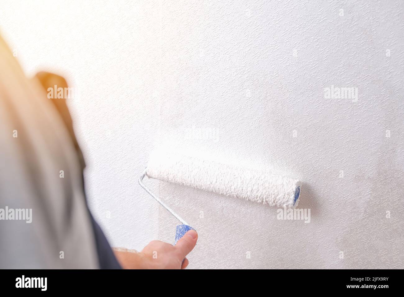 A man is painting vinyl wallpaper with a velour roller for painting