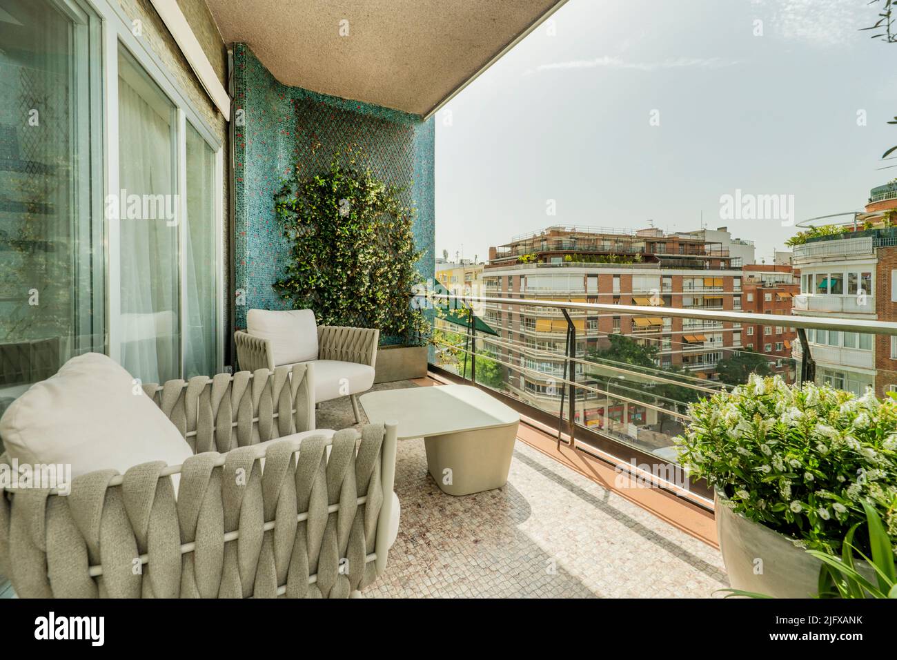 Terrace with gray fabric armchairs, metal railing, planter, vertical garden on a blue wall and views of the city Stock Photo