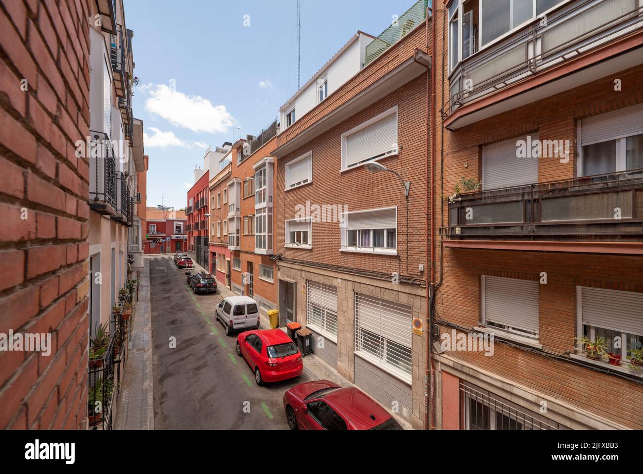 Narrow street with low-rise buildings with clay brick facades with balconies and terraces Stock Photo