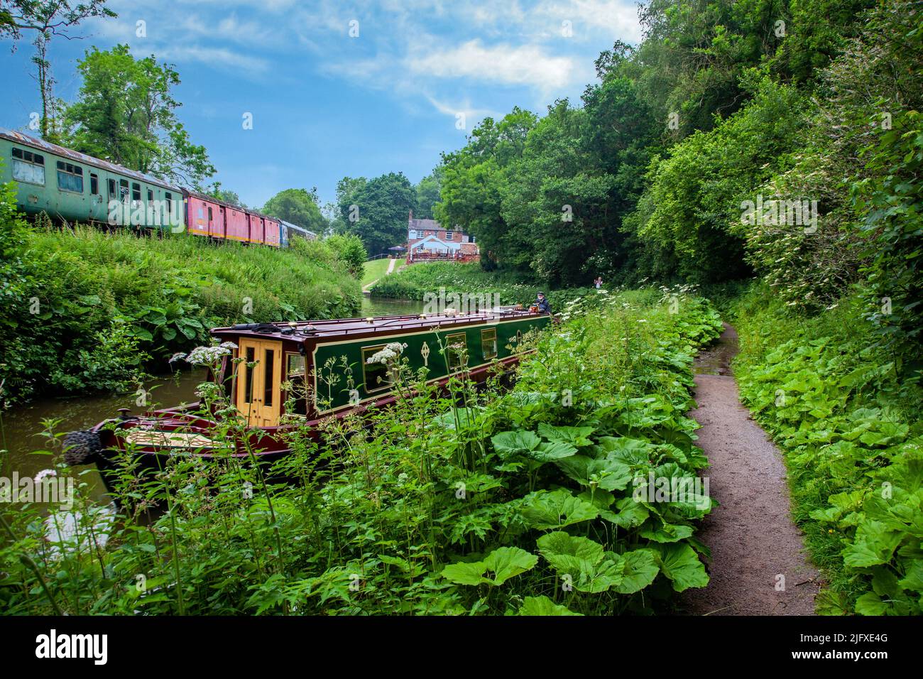 Narrowboat moored on the Caldon canal Staffordshire with a train on the Churnet valley railway in the background Stock Photo
