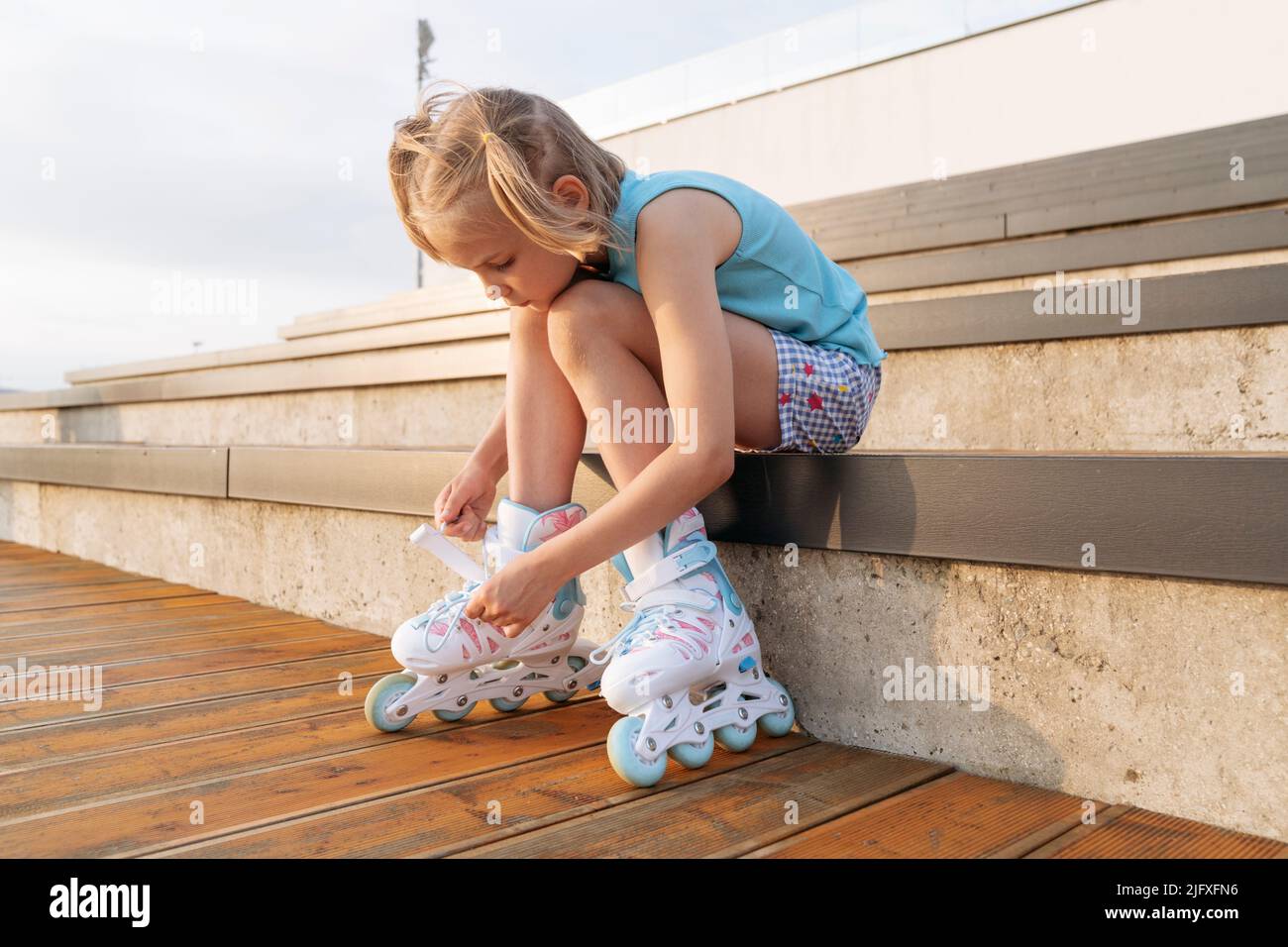 A girl in roller skates sits on a park bench and fastens the lock. Stock Photo