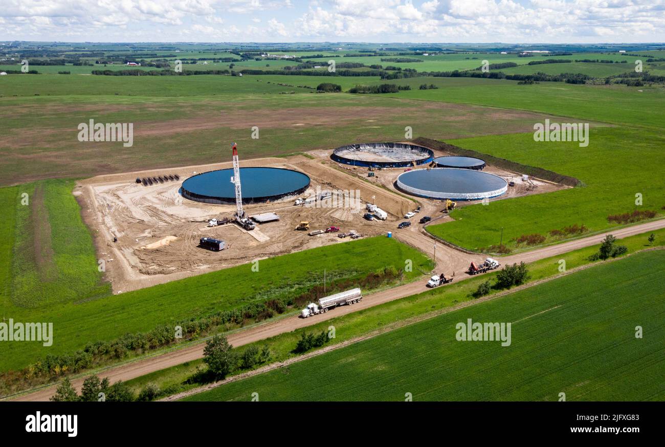 An oil well service rig and storage tanks are seen surrounded by farm