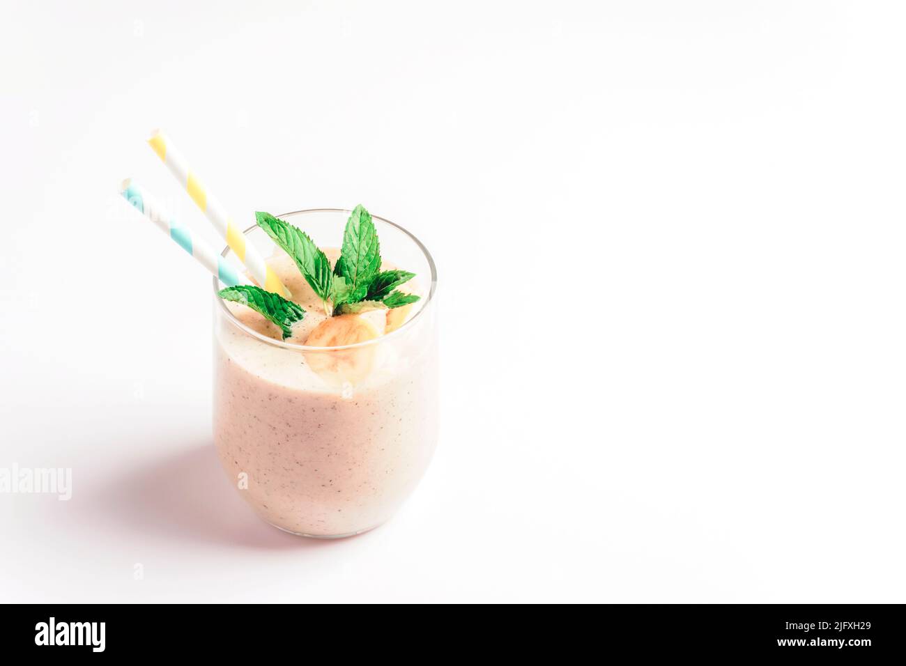 Banana smoothie with straw and mint leaf on white background. Healthy vegan food. Stock Photo