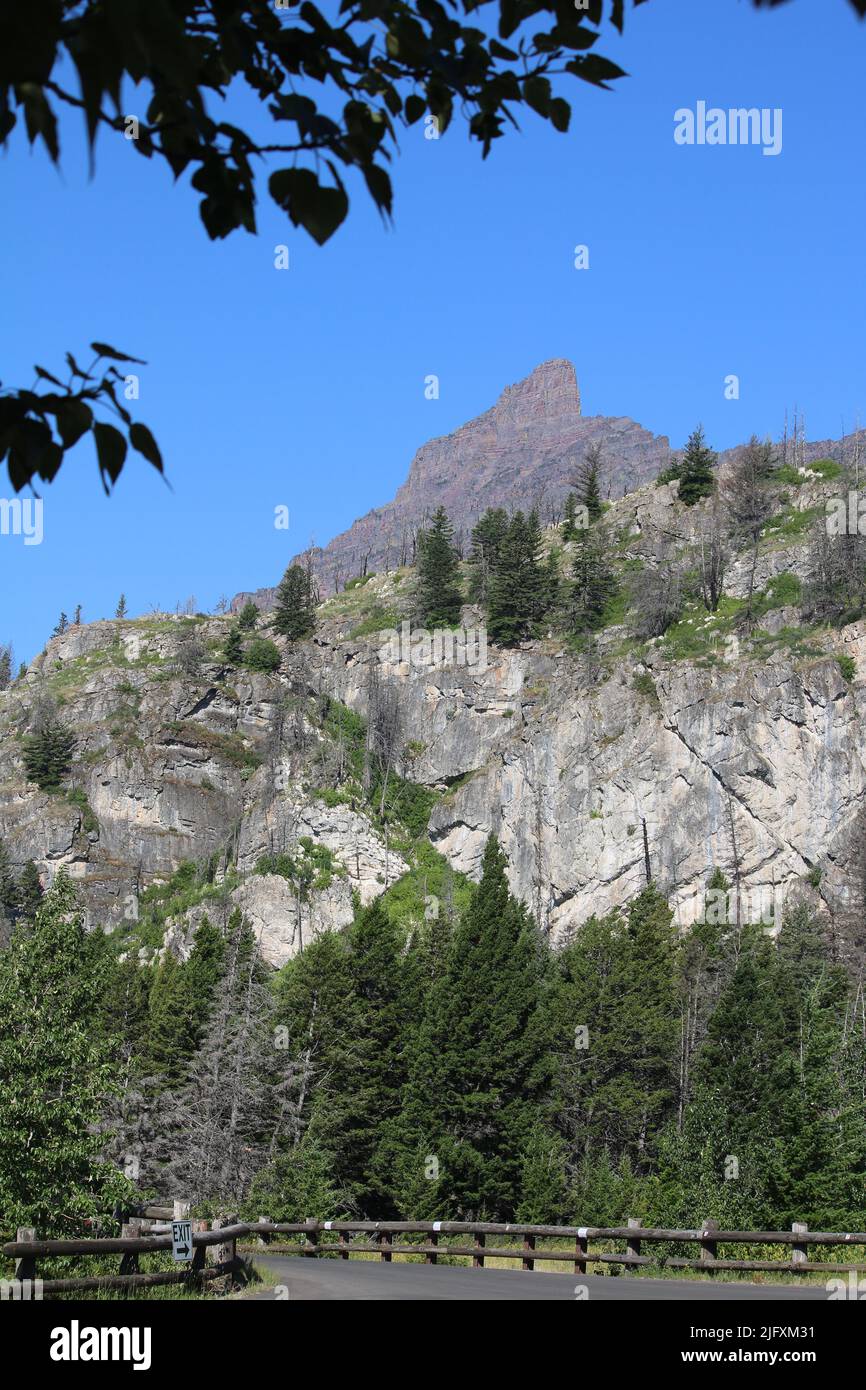 Green leaves & pines frame brilliant blue sky, rich red of Goat Mountain & light-colored limestone, Rising Sun Camp, Glacier National Park, MT, USA Stock Photo
