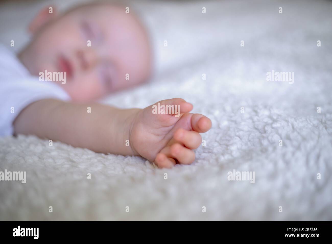 small hand of a sleeping baby on a white blanket. Stock Photo