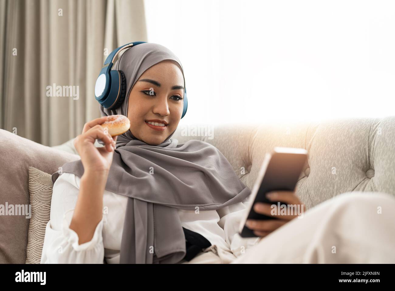 Beautiful Asian muslim woman using mobile phone while sitting on sofa ...