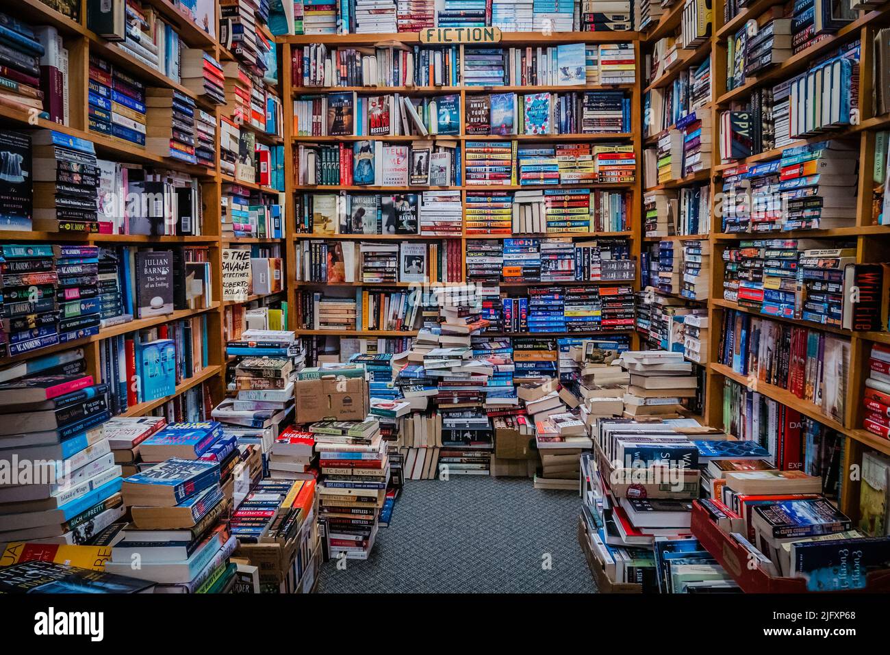 A small room filled with books on shelves and on the floor Stock Photo